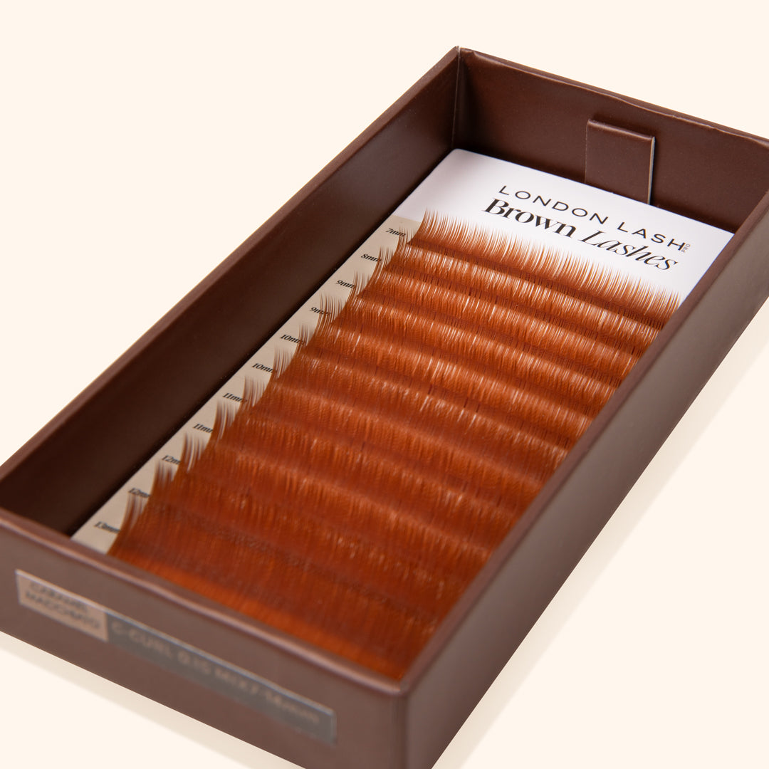 mix tray of brown eyelashes inside an open brown lash tray on beige background